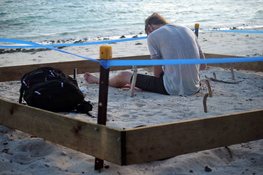 David Adams sits inside a rectangular wooden frame on a white sandy beach