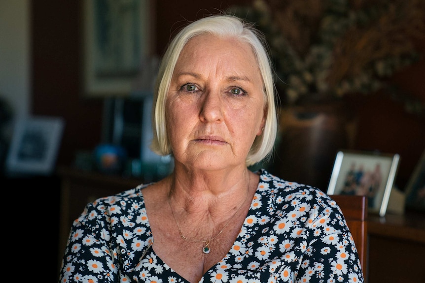 A close up of Yvonne Buters wearing a black shirt with white flowers on it, looking directly into the camera.