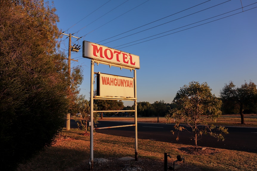 Faded sign on roadside reads Motel Wahgunyah. There are powerlines overhead and early morning sunlight.