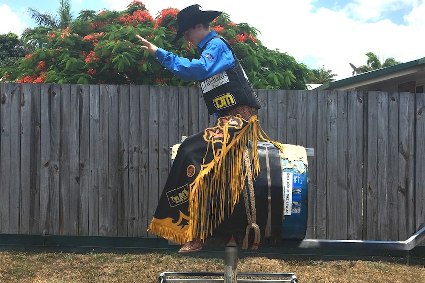 Mackay bull rider Ky Hamilton, 15, practices bull riding on a bucking bull in his backyard.