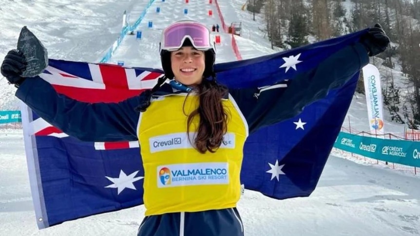 An Australian ski athlete holds her arms wide with a national flag as she celebrates a win