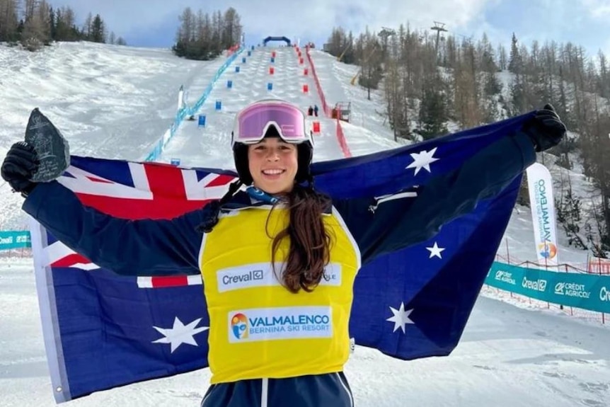An Australian ski athlete holds her arms wide with a national flag as she celebrates a win