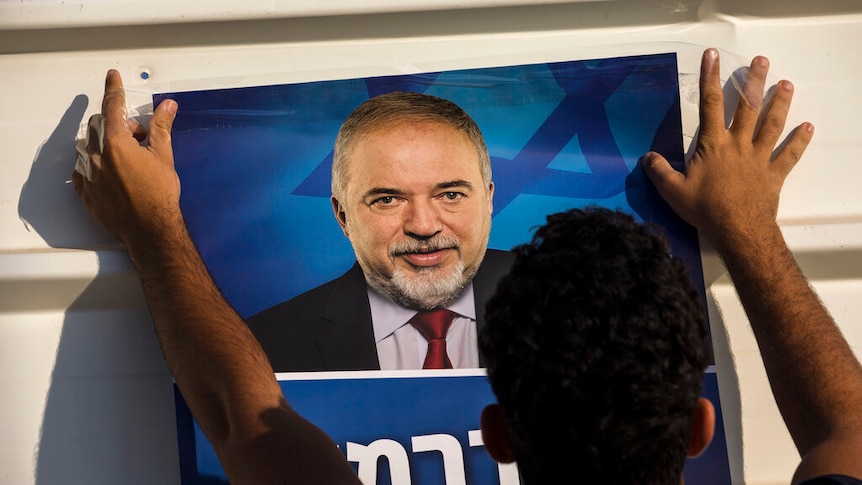 Against a white corrugated iron wall, a man tapes a poster of Avigdor Lieberman, the leader of Israel's Yisrael Beiteinu party.