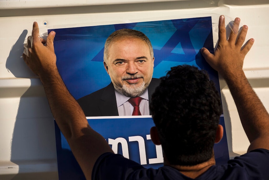 Against a white corrugated iron wall, a man tapes a poster of Avigdor Lieberman, the leader of Israel's Yisrael Beiteinu party.