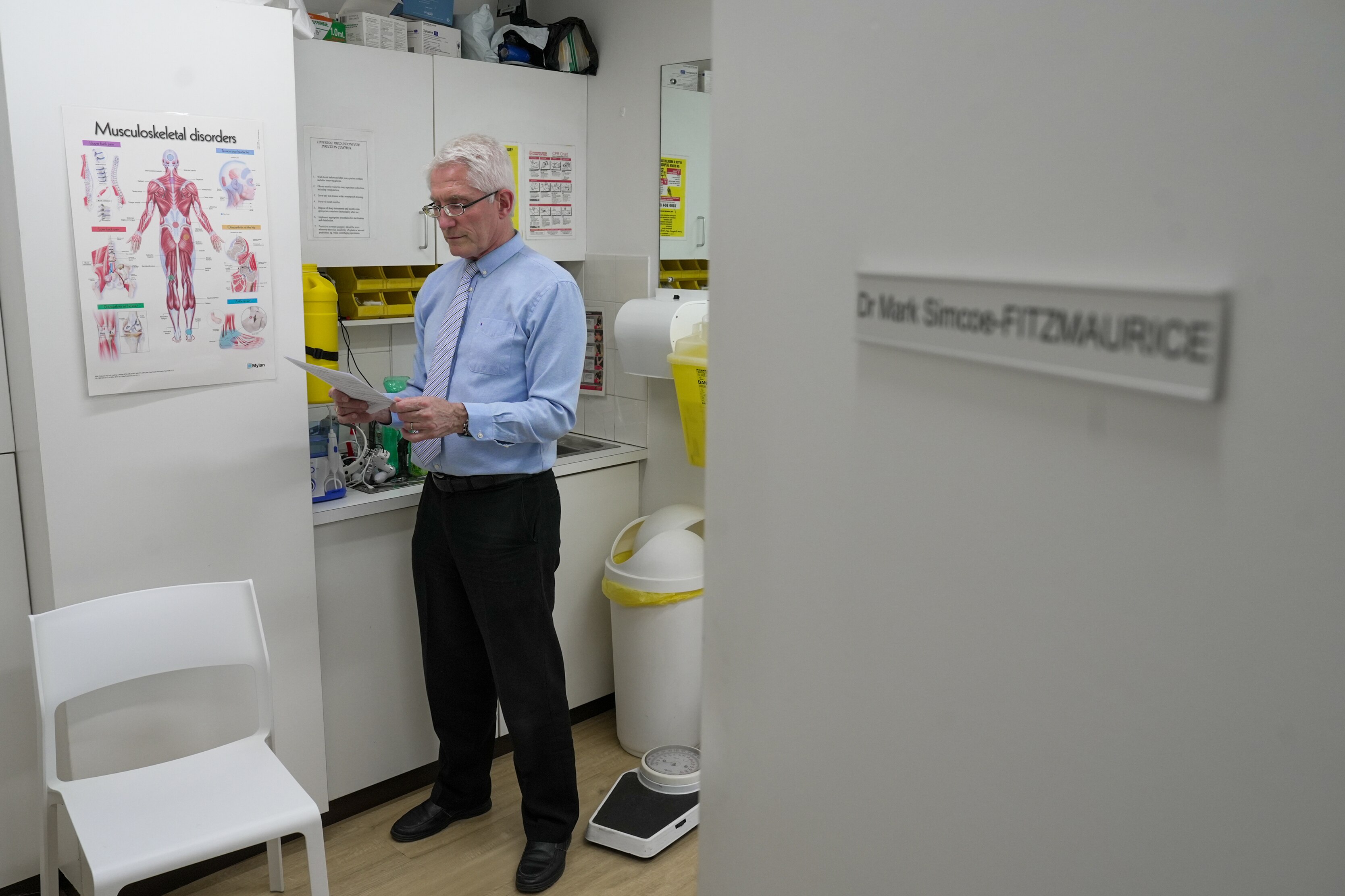 A doctor reviews paperwork in his room. His name is on the door.