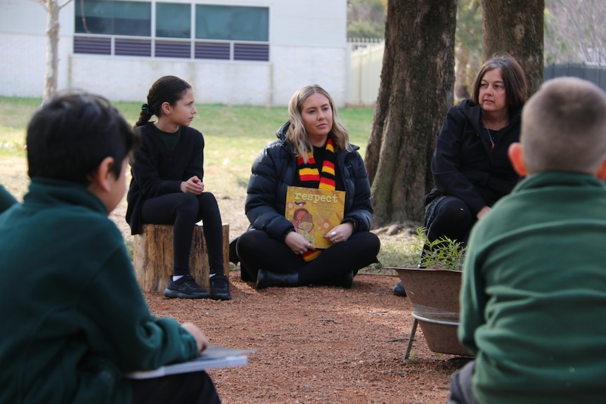 A woman sits in a school yard surrounded by school students