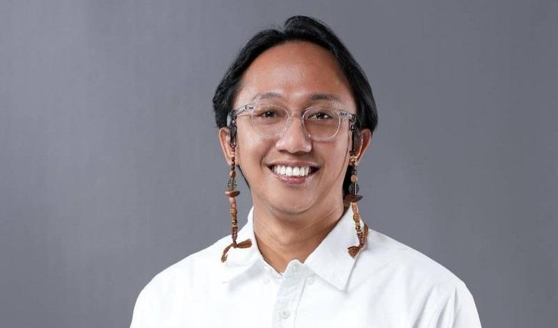 Wana, a man in glasses smiling to camera against a grey background.