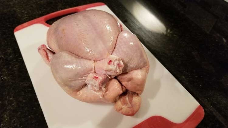 raw chicken tied with string on chopping board