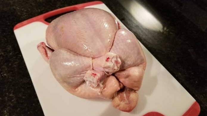 raw chicken tied with string on chopping board