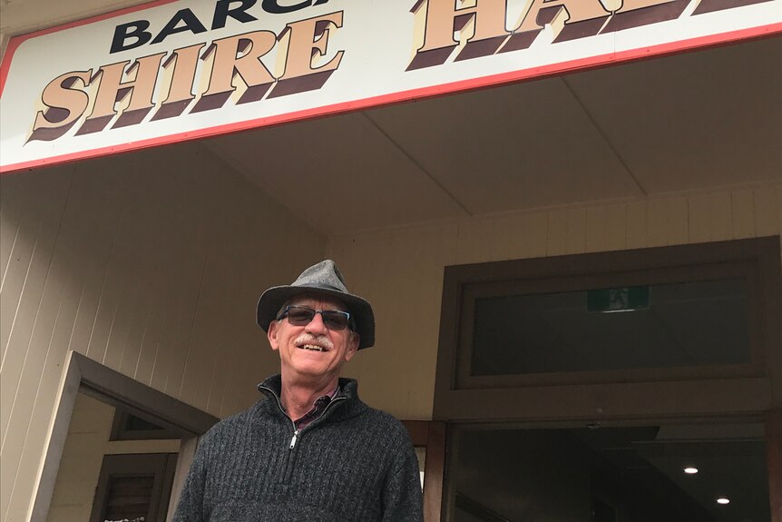 A man wearing a dark jumper, a grey trilby hat and sunglasses standing outside the Barcaldine Shire Hall