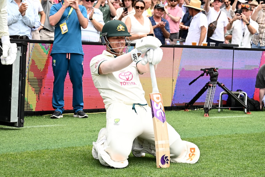 David Warner leans back while on his knee, holding his cricket bat