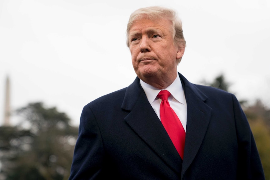 US President Donald Trump wearing a black coat with a red tie listens to questions