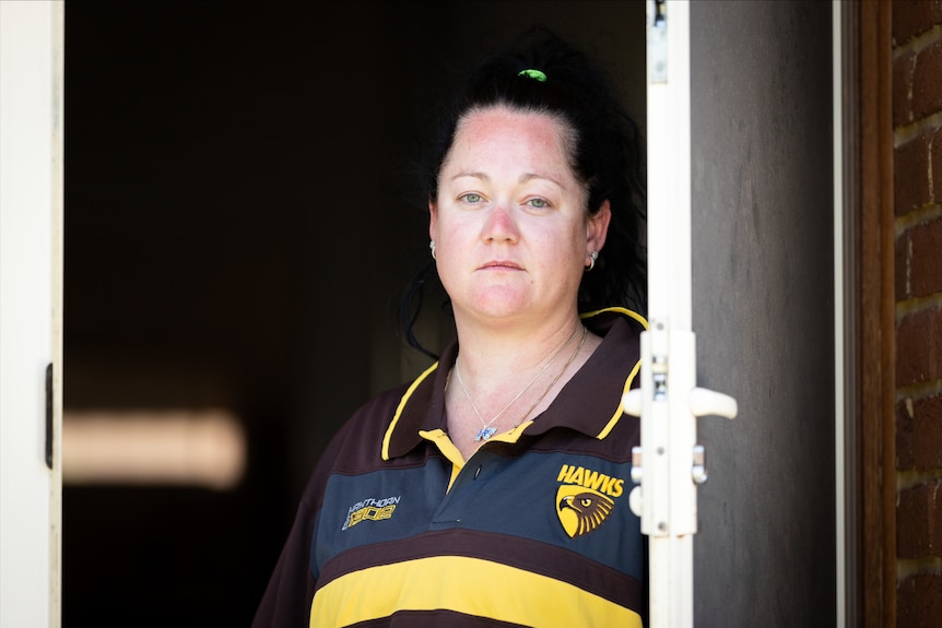 A head and shoulders picture of a woman wearing a Hawthorn shirt standing in a doorway posing for a photo.