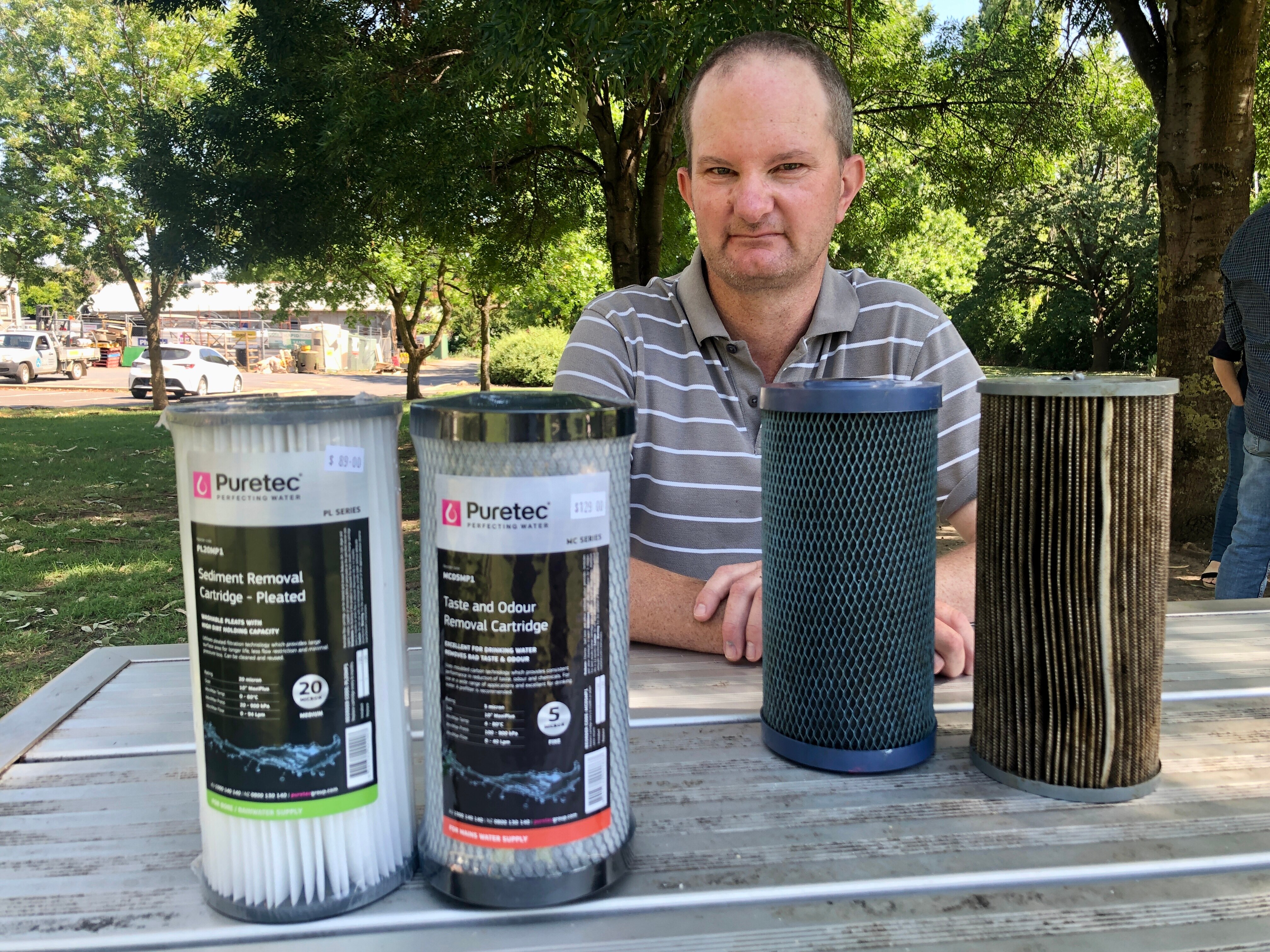 A man sitting at a picnic table with new and used water filters.