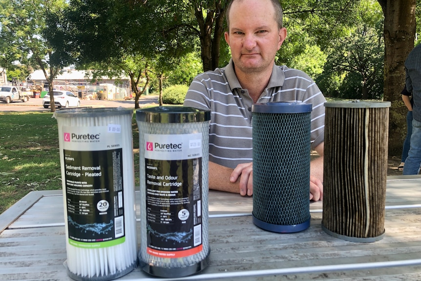 A man sitting at a picnic table with new and used water filters.