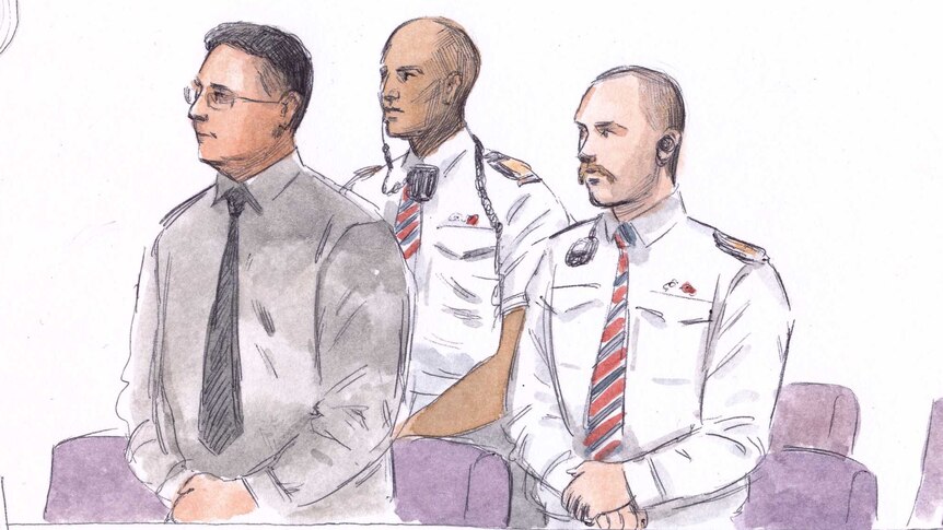 A court sketch of a man with glasses standing in the dock next to two security guards.