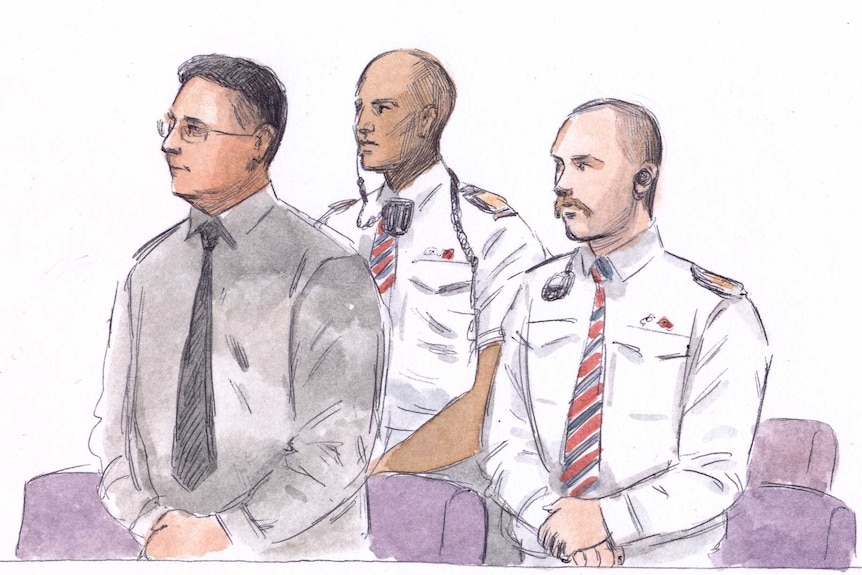 A court sketch of a man with glasses standing in the dock next to two security guards.