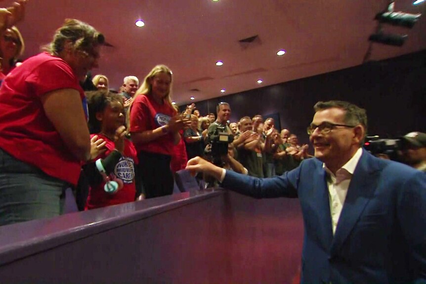Dan Andrews walks past people in Labor shirts, who are clapping.