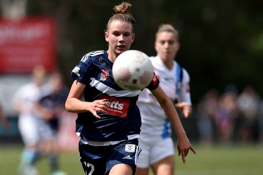 A young woman chases after a soccer ball flying through the air.