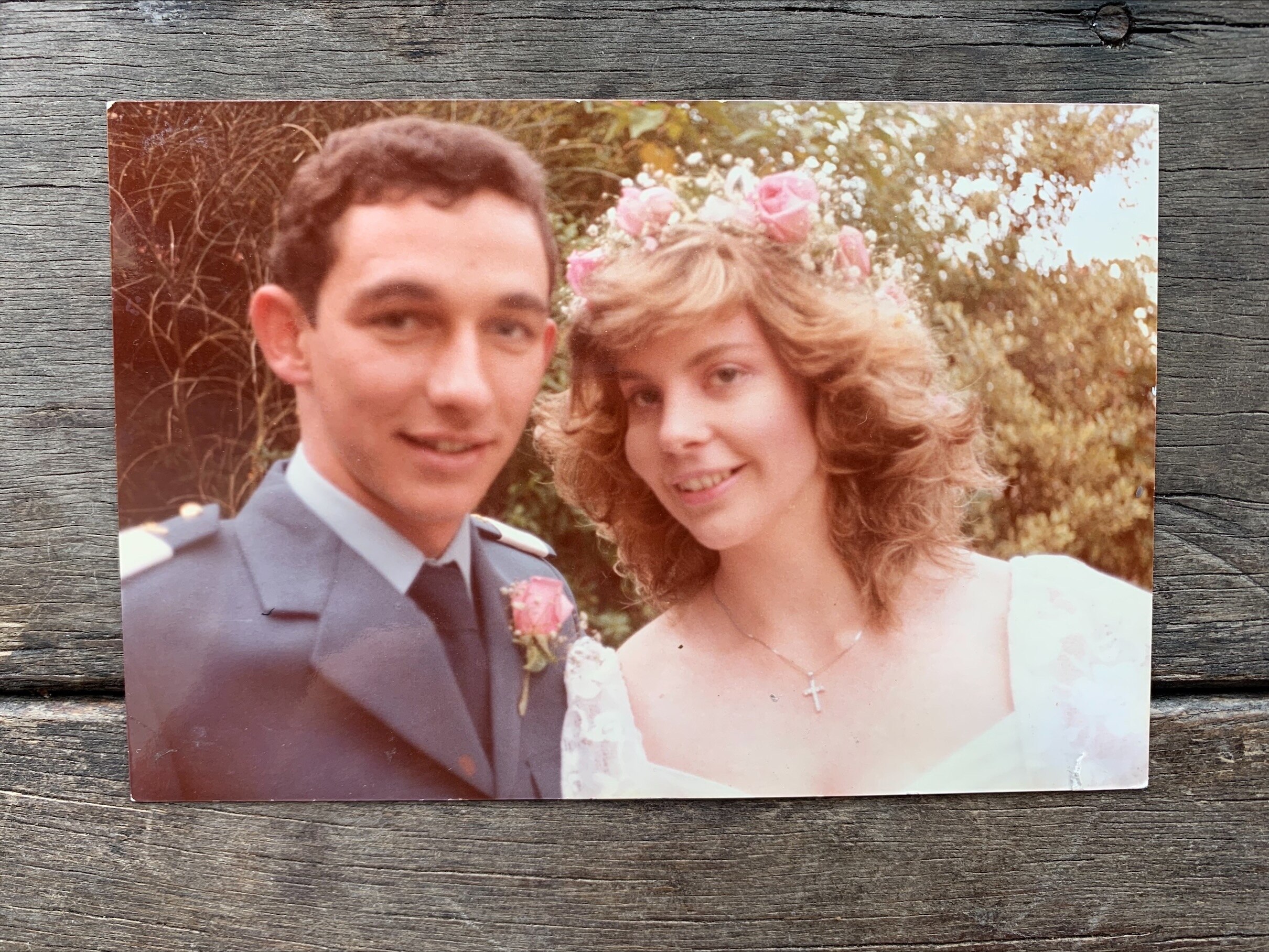 A photograph shows a bride and groom smiling together, bride wearing a crucifix necklace and pink roses in her hair