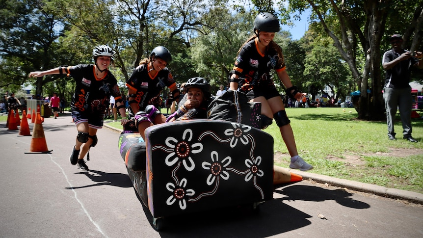 teenagers wearing helmets race a couch on the street