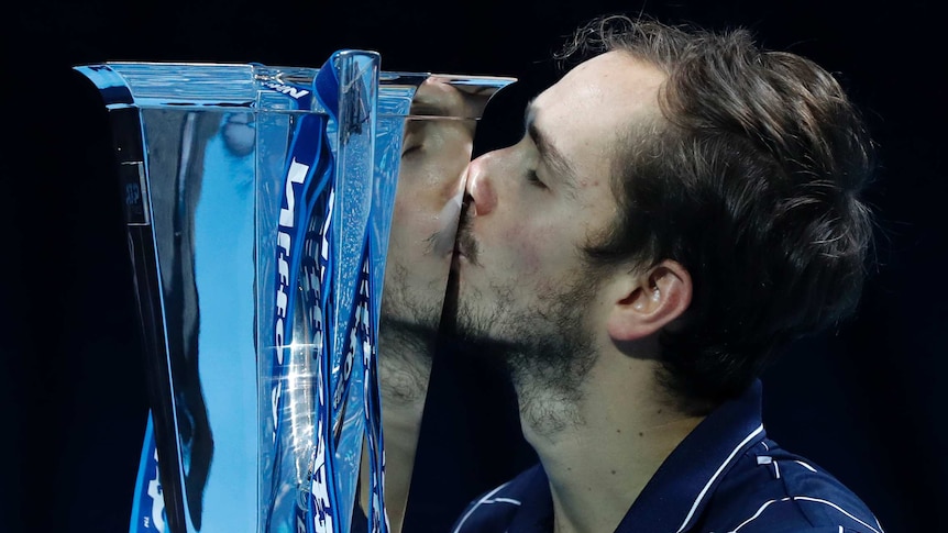 Daniil Medvedev kisses a reflective silver trophy with his eyes closed