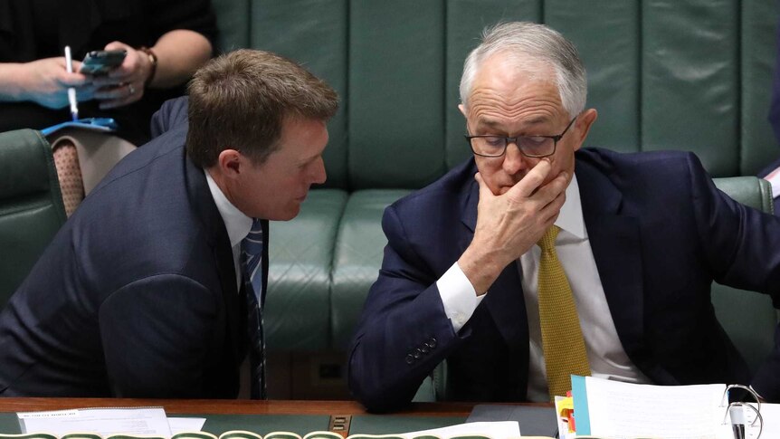 Mr Turnbull has his hand over his mouth as Mr Porter talks to him.