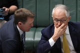 Mr Turnbull has his hand over his mouth as Mr Porter talks to him.