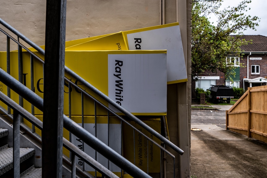 A bunch of yellow rental signs leaning up against a wall and staircase at the back of a building