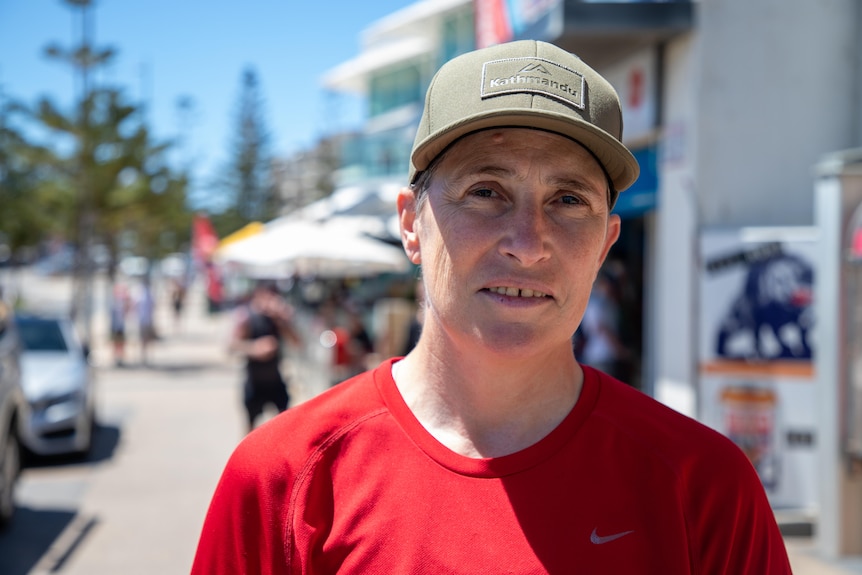 A woman in a hat and red shirt poses for a photo at a beach 