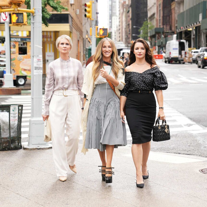 Three women stand on the pavement in New York City smiling at the camera