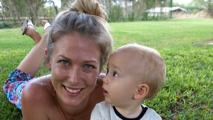 A young woman lies on the grass with her baby