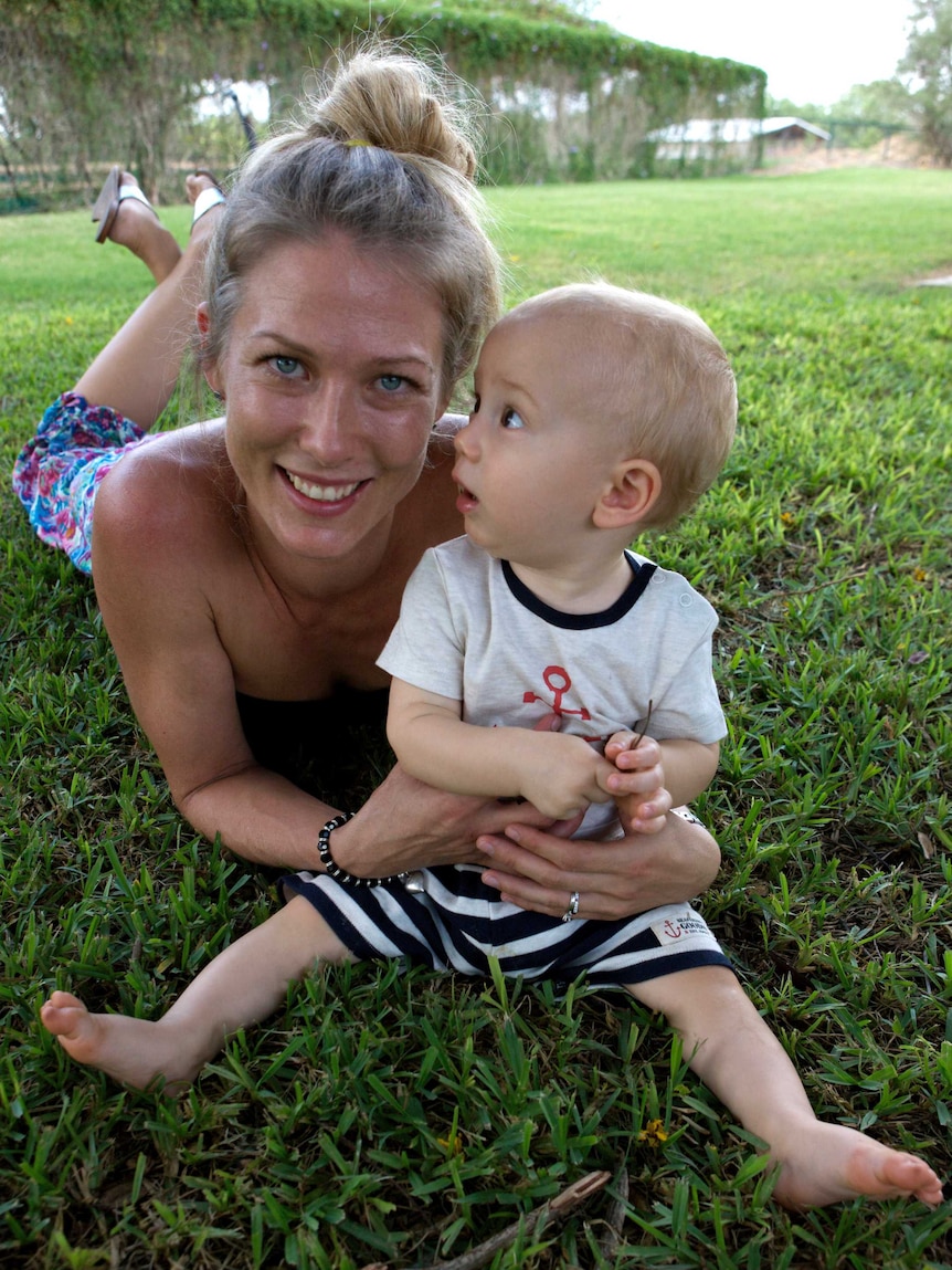 A young woman lies on the grass with her baby