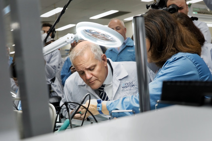 Morrison Peers Down At A Microchop Under A Bright Light That Looks Like A Halo Above His Hear