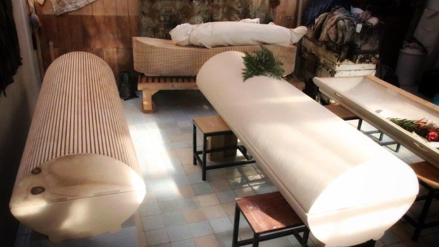 Four biodegradable coffins displayed on a patio. They are made of recycled paper and plywood