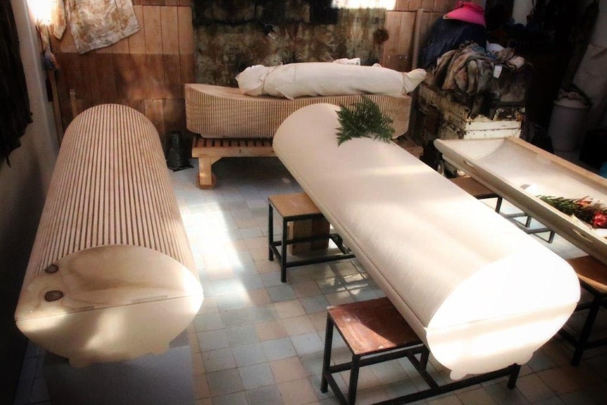 Four biodegradable coffins displayed on a patio. They are made of recycled paper and plywood
