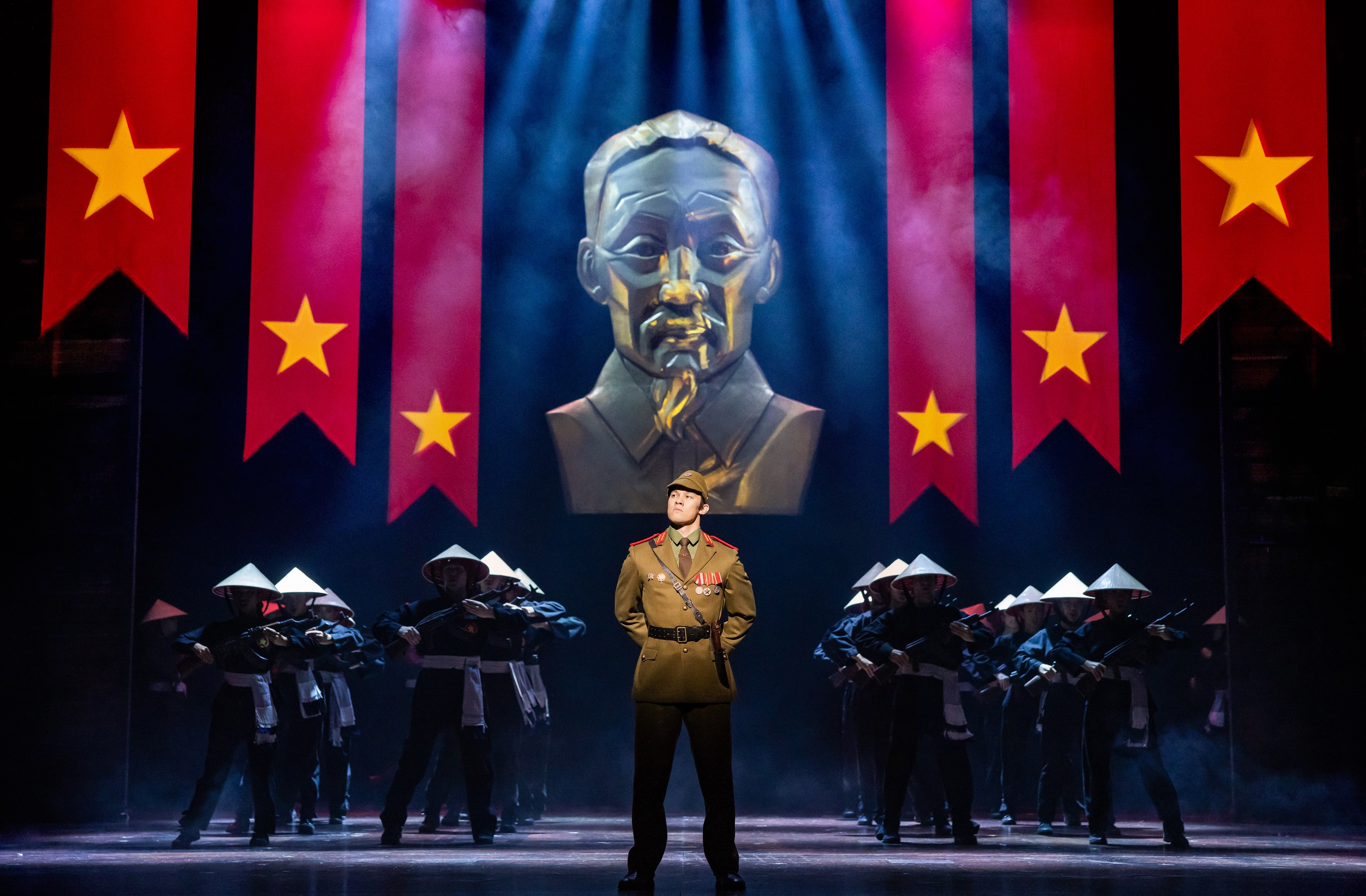 A photo of a stage production with soldiers, a giant gold bust and red flags with yellow stars