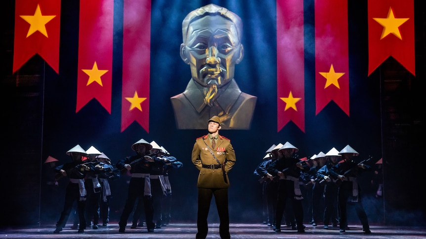 A photo of a stage production with soldiers, a giant gold bust and red flags with yellow stars