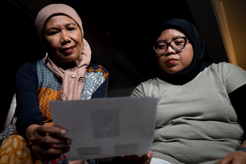 Two Indonesian women sit in a dark room looking at a photograph