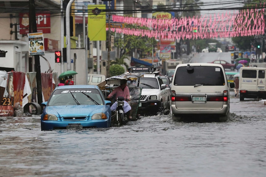 Cars and motorbikes drive through a flooded street in Quezon city.