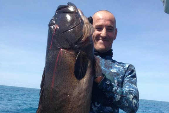 a man stands in a wetsuit holding a big fish
