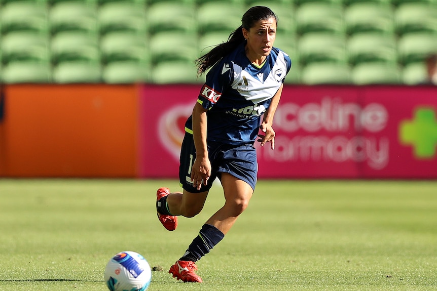 A soccer player wearing navy blue and white runs towards the ball