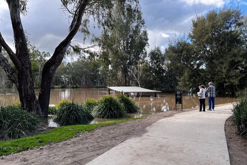 Two people stand on the banks of a flooded river.