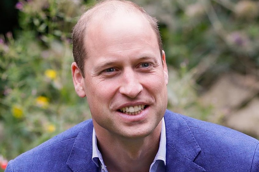 Prince William smiles at the camera while sitting in a garden.