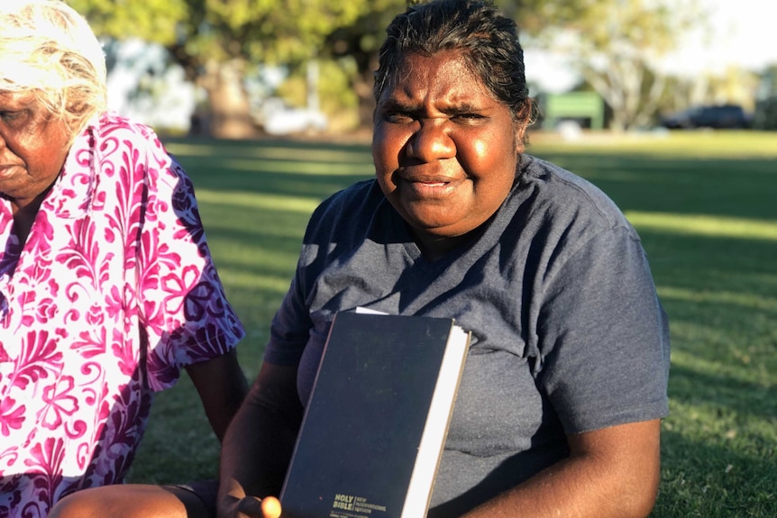 Sandra Cox, and Aboriginal woman, holding a Bible. She is sitting a park.