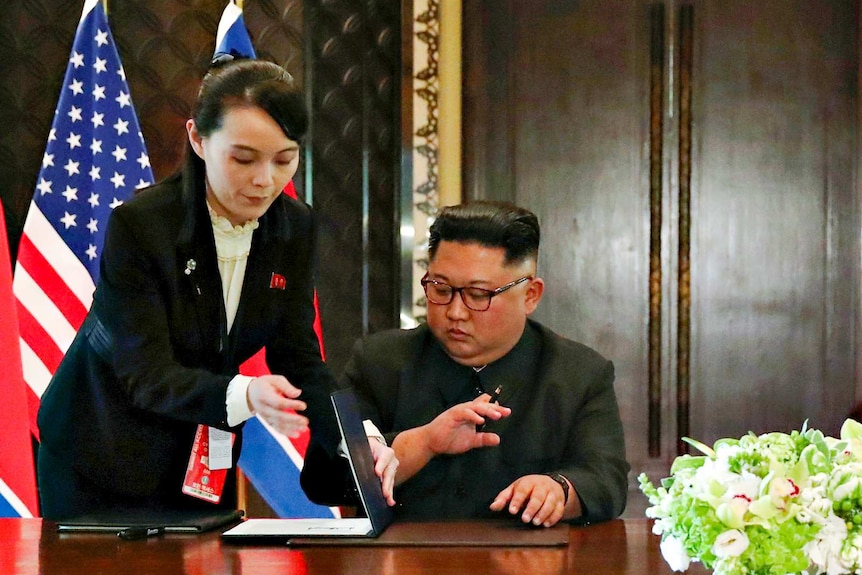 Kim Jong-un sitting at a table while his sister Kim Yo-jong opens up a fo.....