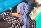 Woman wearing a purple hijab looking out at a street in the evening, with brush strokes around her.