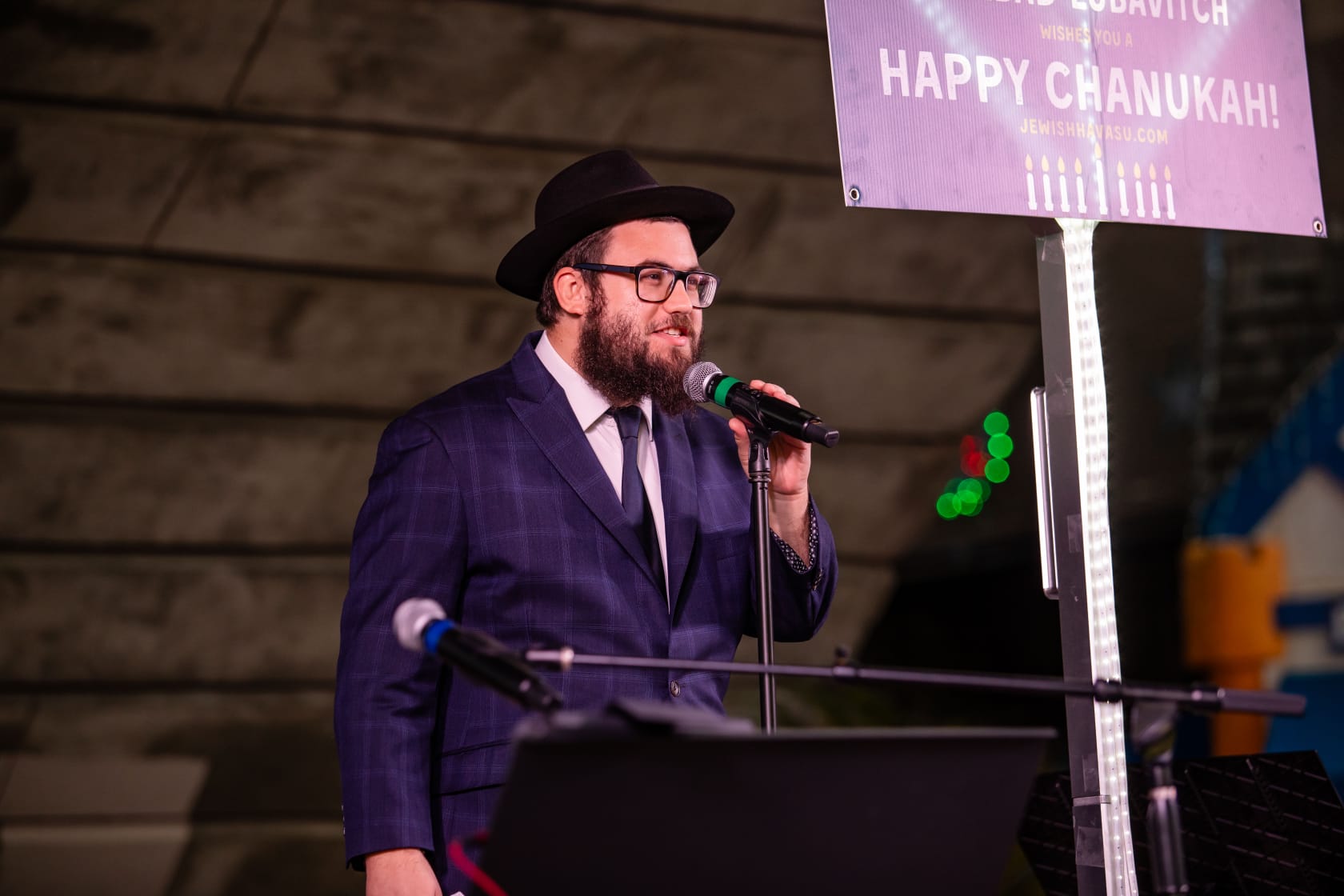 El rabino Mendel Super está parado en un podio y sostiene un micrófono.