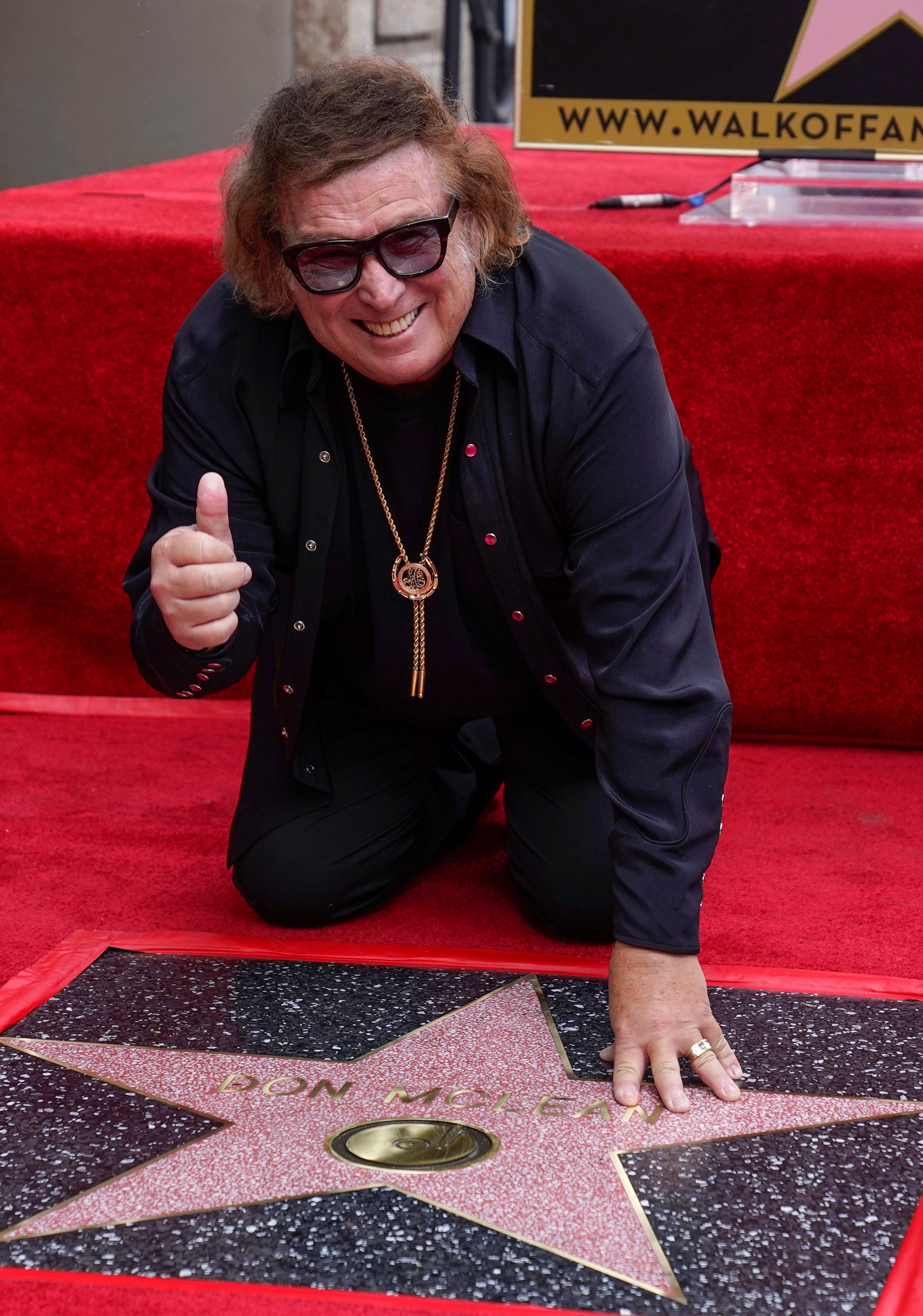 Don McLean gives a thumbs-up as he kneels over his star on the Hollywood Walk of Fame.