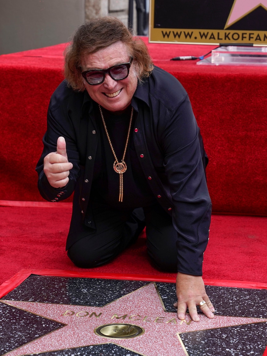 Don McLean gives a thumbs-up as he kneels over his star on the Hollywood Walk of Fame.